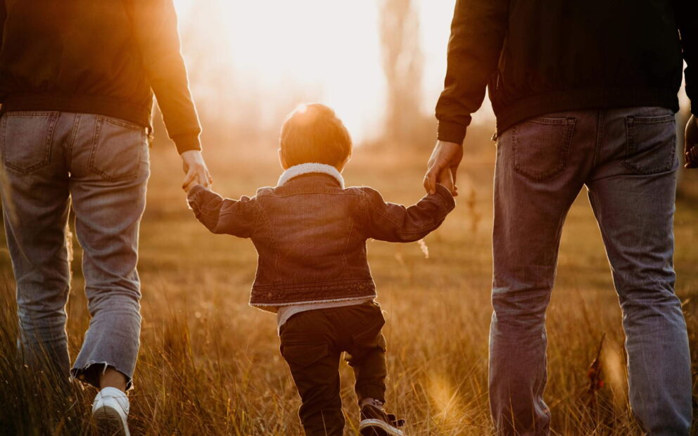 Familie mit Kind Hand in Hand spazierend im Sonnenuntergang