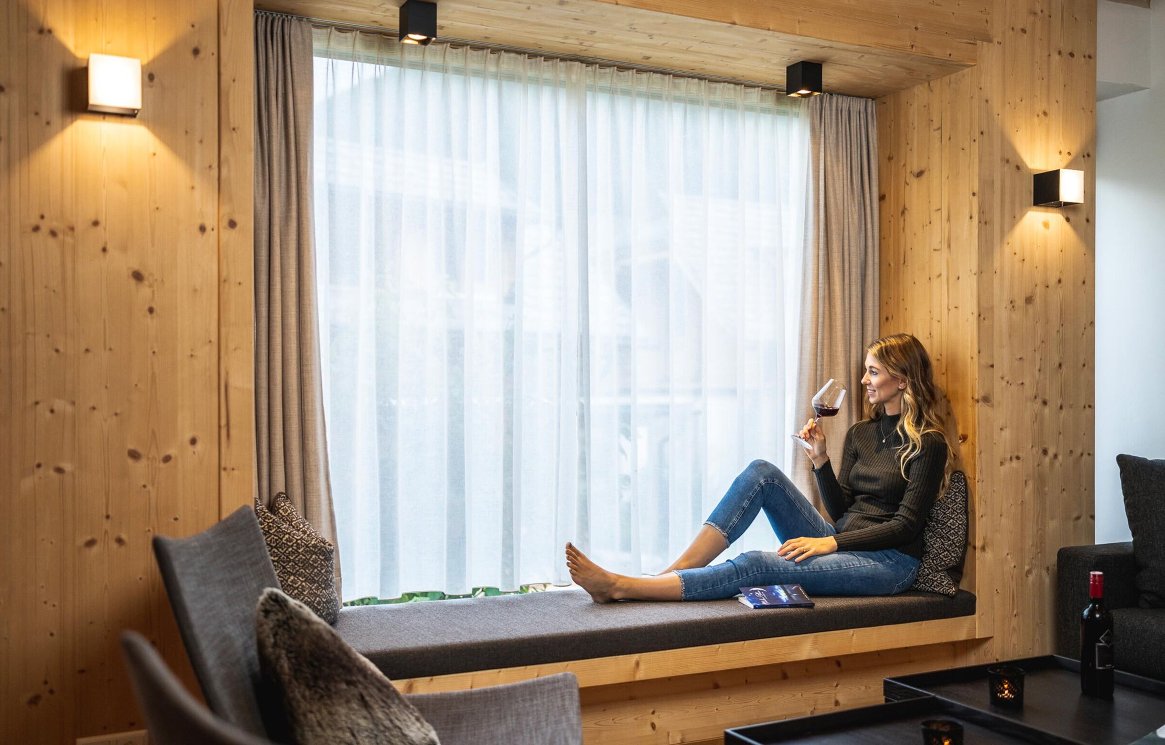 Frau mit einem Glas Wein bei dem Panoramafenster der Trattler Hof-Chalets