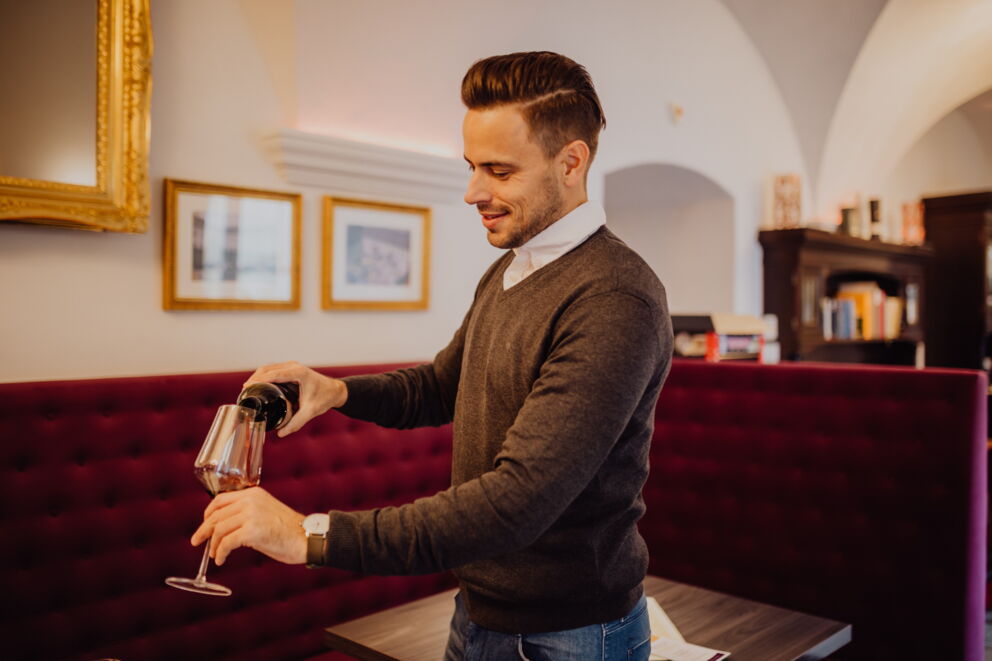 A man who pours a glass of red wine while standing and smiling