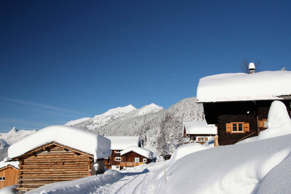 Beschneite Winterhüttensiedlung mit Blick auf beschneite Gebirgszüge in Vorarlberg
