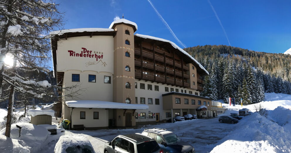 Ansicht auf das verschneite Hotel der Rinderhof, mit Blick auf die verschneite Berglandschaft
