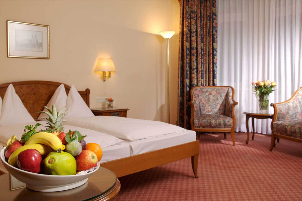 Gemütliches Zimmer mit rotem Teppichboden, großem Bett und einer vollen Schüssel Obst