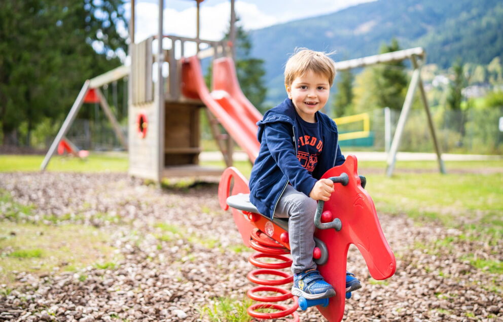 Fröhlicher kleiner Junge am Spielplatz auf einem Schaukelpferd