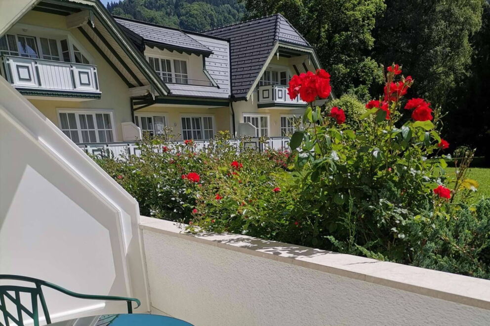 Balkon geschmückt mit roten Blumen und Sicht auf den Seehof Mondsee