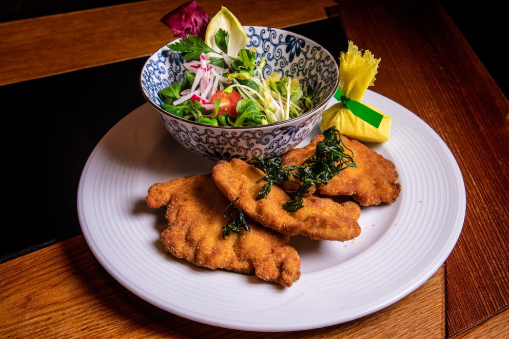 Drei Stück Backhendl auf einem Teller mit einer Schüssel gemischtem Salat