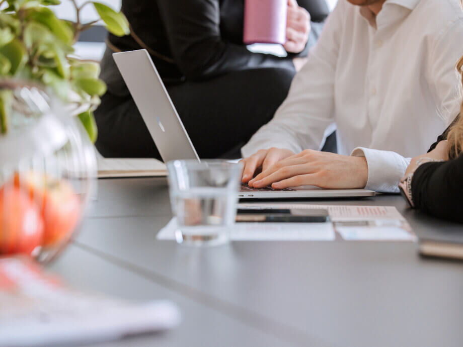 Hände tippen auf einem Laptop während eines geschäftlichen Meetings am Tisch mit Wasser und Dokumenten.