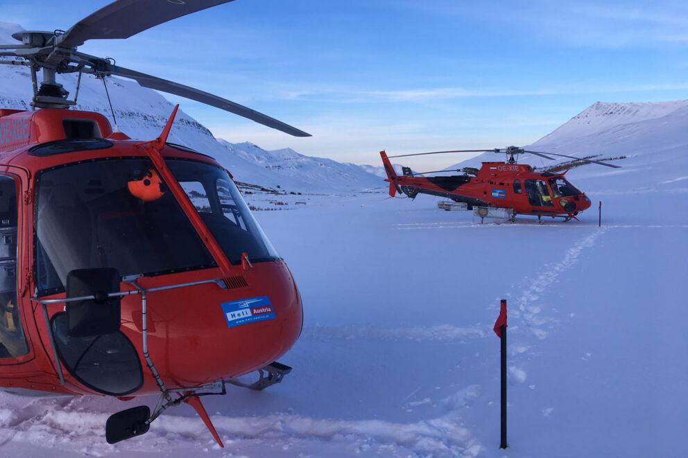 Zwei rote gelandete Hubschrauber auf verschneitem Gebirgszug