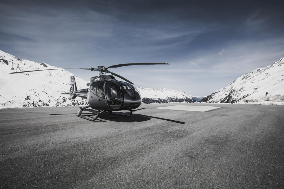 Schwarzer Helikopter auf einem Landeplatz mitten umschlossen von verschneiter Berglandschaft
