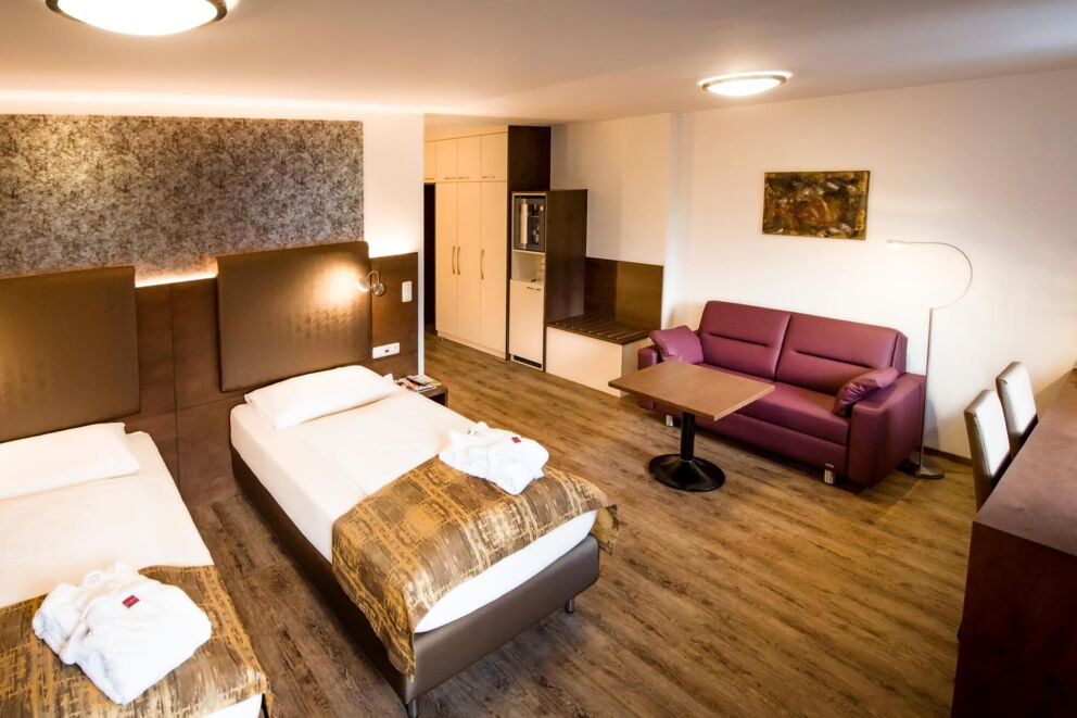 geräumiges Zimmer mit 2 Einzelbetten und einer roten Couch im Hotel der Kaiserhof