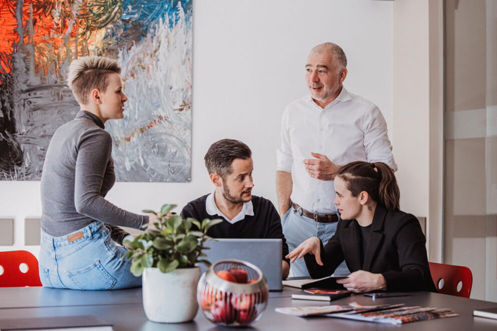 Eine Gruppe von vier Fachleuten diskutiert um einen Laptop in einem modernen Büro.
